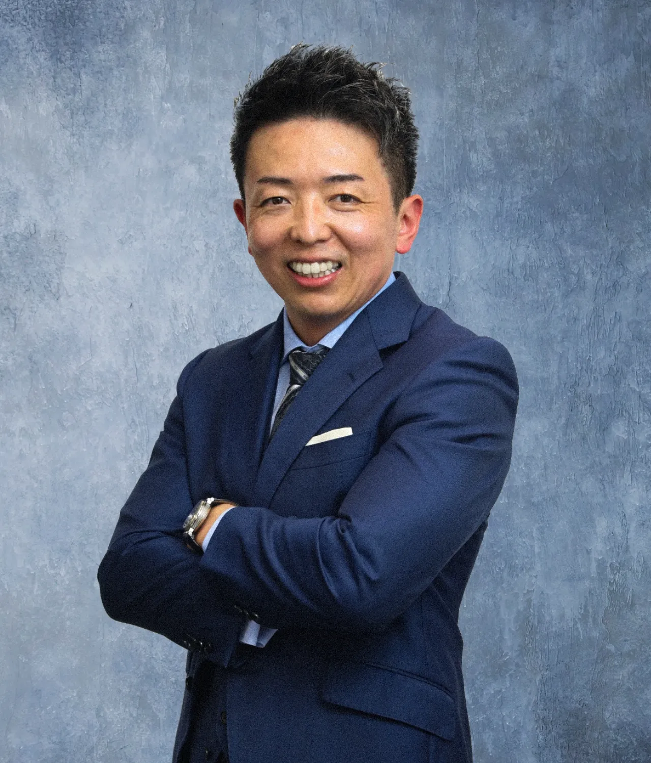 腕を組み、自信に満ちた表情で微笑む紺色のスーツを着た男性役員。