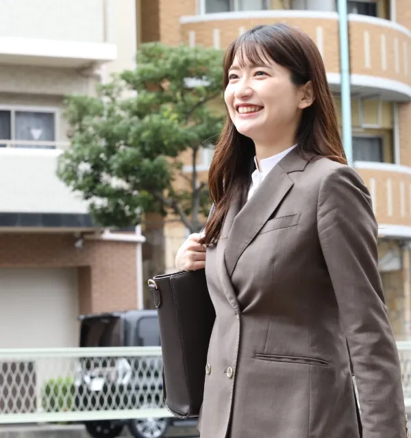 茶色のスーツを着て、バッグを肩にかけ、屋外を笑顔で歩くビジネスウーマン。