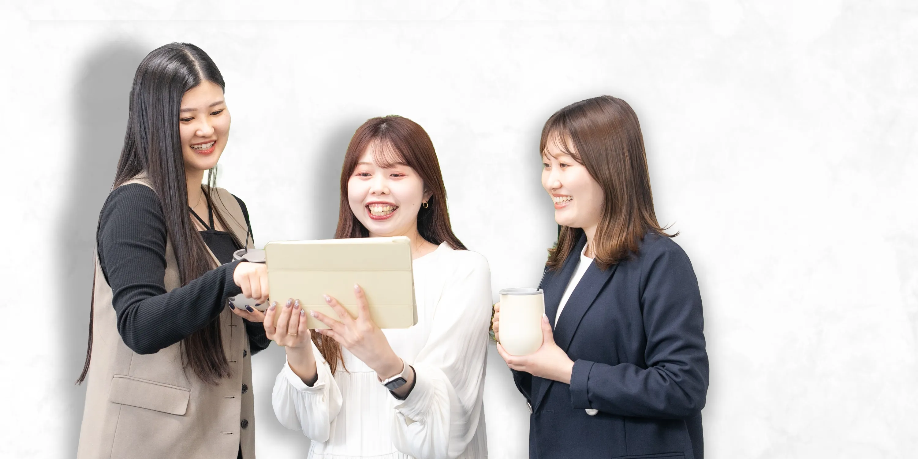 白い背景の中で、タブレットを見ながら楽しそうに打ち合わせをする3人の女性社員。