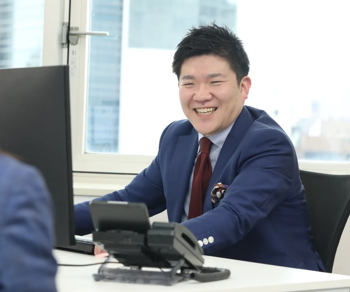 デスクで電話の横に座り、明るい笑顔でコミュニケーションを取る男性社員。