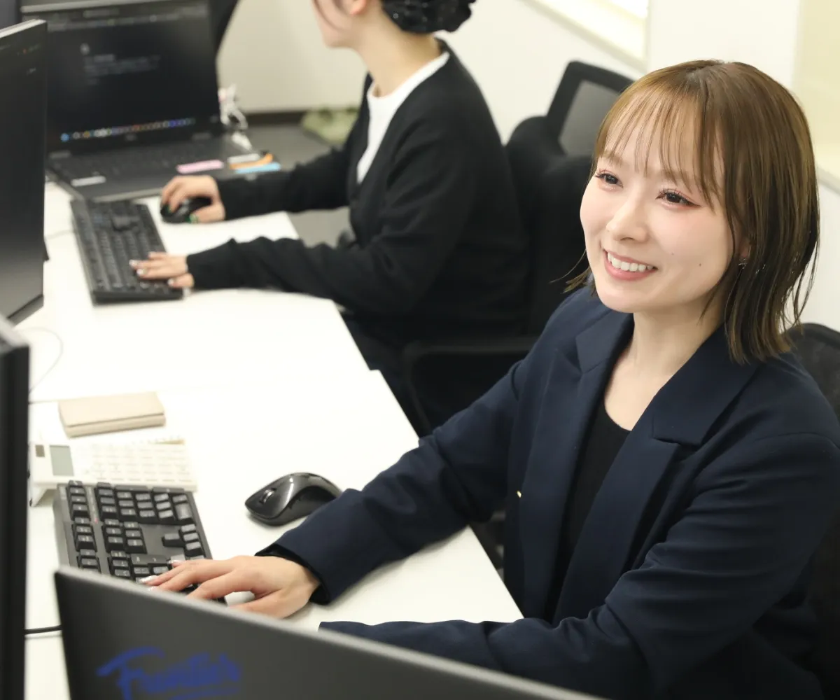 パソコン作業をしながら、同僚と楽しそうに話す笑顔の女性社員。