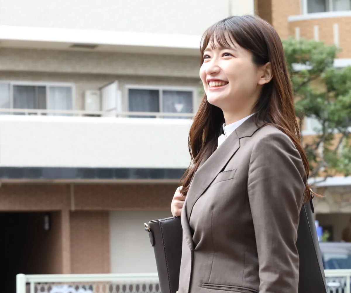 屋外を歩きながら、前向きな表情で遠くを見つめるスーツ姿の若手女性社員。