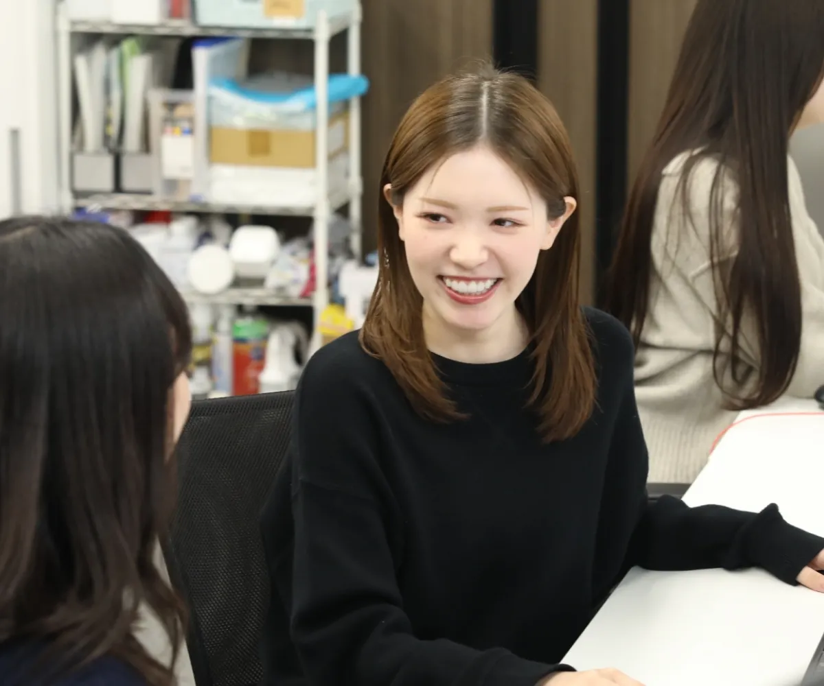 黒いセーターを着て、リラックスした雰囲気で会話を楽しむ笑顔の女性社員。