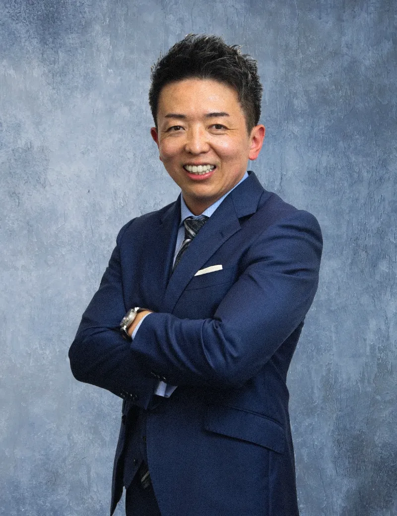 腕を組み、自信に満ちた表情で微笑む紺色のスーツを着た男性役員。