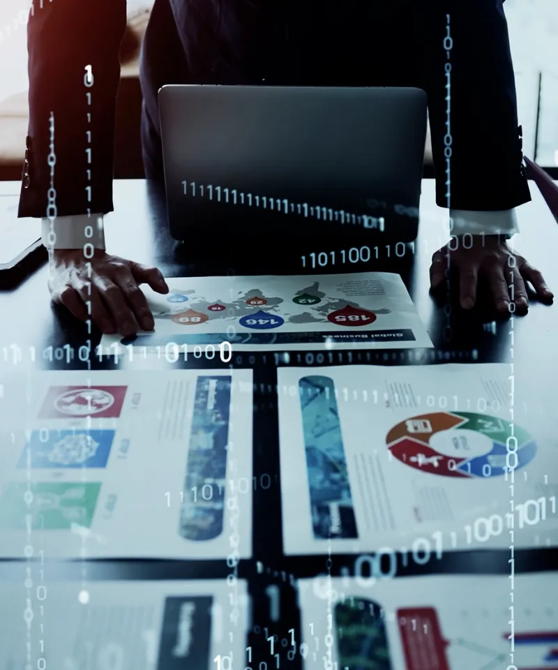 デスク上のビジネス資料（地図、円グラフ）に手を置くスーツ姿の人物と、重なり合って流れるデジタルのバイナリコード（0と1）。DXやデータ分析をイメージしたサイバーな描写。