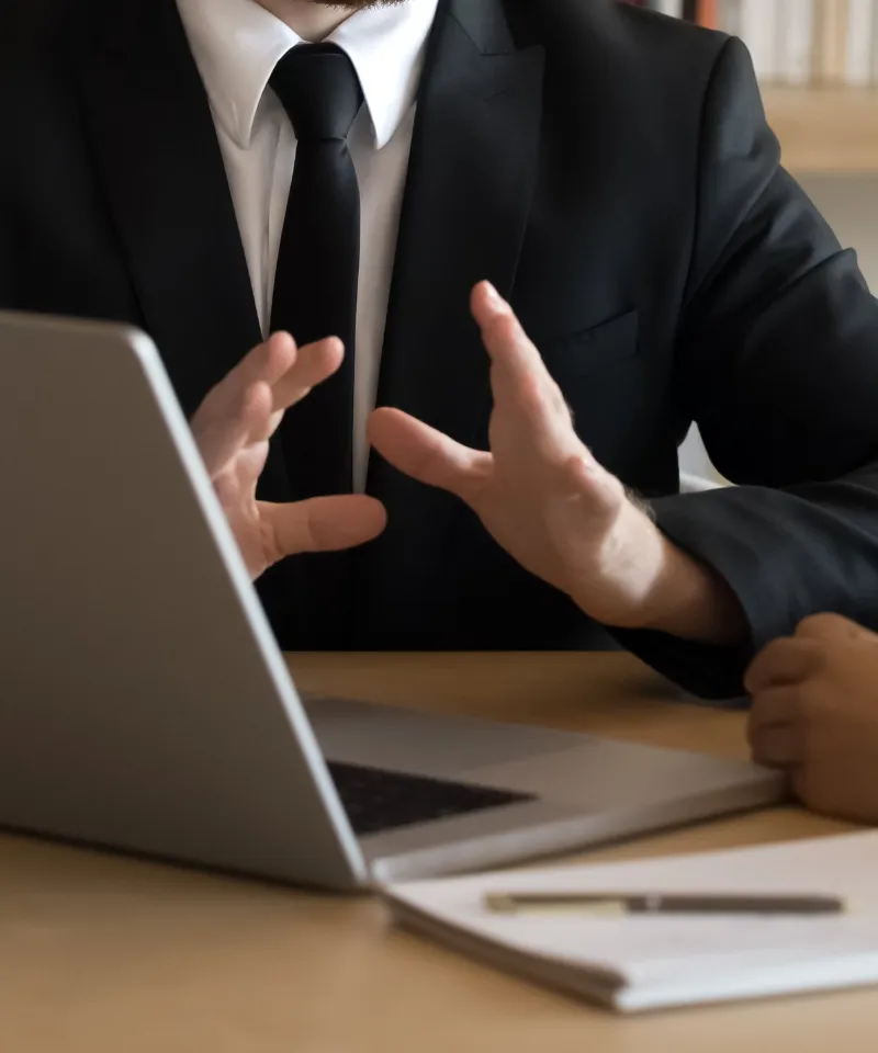 商談や打ち合わせで、ノートパソコンを前に身振り手振りで熱心に説明するビジネスマン。