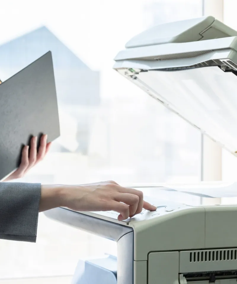 オフィス内の複合機で書類のスキャンやコピー作業を行う事務スタッフの手元。